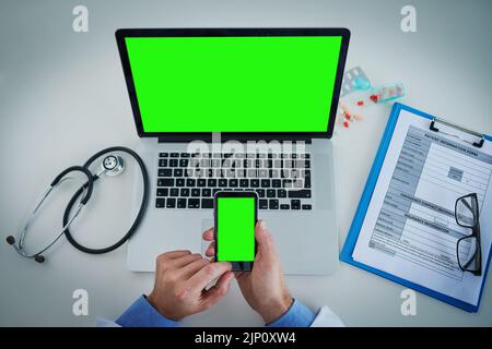 Every medical professional needs to stay updated. High angle shot of an unrecognizable doctor using a laptop and cellphone with a green screen in his Stock Photo