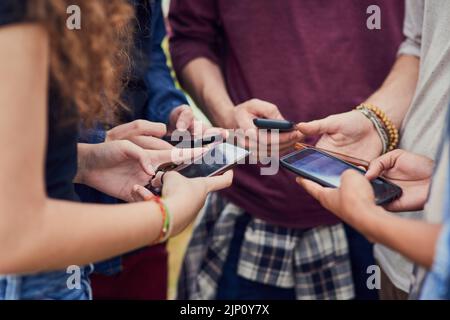 Living in a age of technology. a group of young unrecognizable people standing in a circle while browsing on their mobile phones outside during the Stock Photo