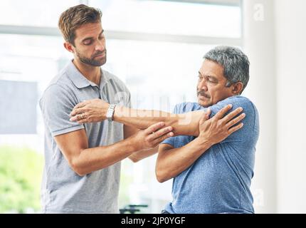 Stretch for me. a young male physiotherapist assisting a senior patient in recovery. Stock Photo