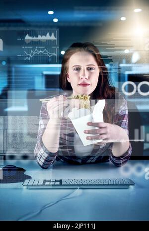 Having a quick snack before climbing back into work. Portrait of a focused young female programmer working on a computer while eating noodles in the Stock Photo