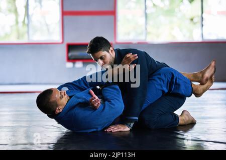 Ground and pound. Full length shot of two young male athletes sparring on the floor of their dojo. Stock Photo