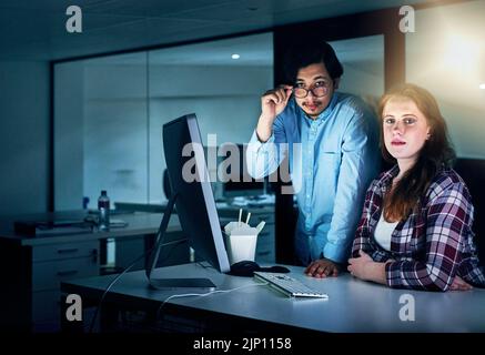 We work long hours to get the work done. Portrait of two focussed young programmers working together on a computer in the office at work during the Stock Photo