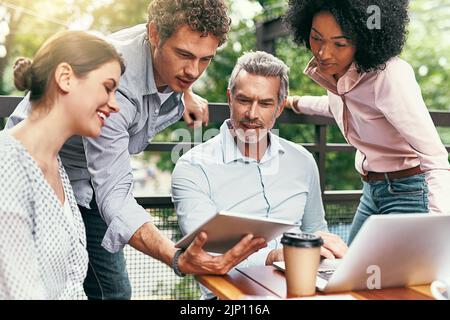 Hosting their quarterly management meeting outside. a team of colleagues using a laptop and digital tablet together during a meeting outdoors. Stock Photo