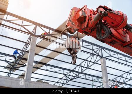 Crane hook for lifting with roof sheet on the steel roof structure at the construction site. Install a new roof. Stock Photo