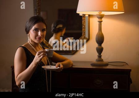 Beautiful woman in black beaded 1920s flapper dress looking into her antique mirror Stock Photo