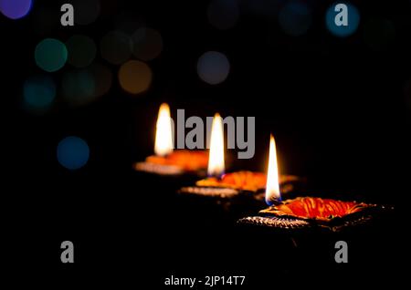 Selective focus on flame of clay diya lamps lit on dark background with colorful bokeh lights. Diwali festival concept. Stock Photo