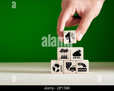 Climate change, environmental pollution and global warming concept. Hand puts climate change symbols on wooden cubes. Stock Photo