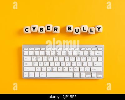 The word cyber bully with computer keyboard on yellow background. Cyber bullying and security concept. Stock Photo