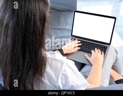Laptop mock up, young woman sitting on the sofa holding laptop mock up. Woman relaxing, online learning, reading news, typing, white blank screen. Stock Photo
