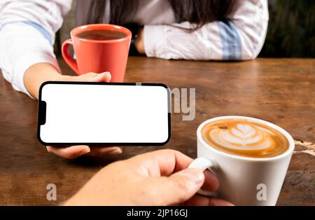 Holding smartphone, young woman holding smartphone. Young couple sitting in the coffee shop. Caucasian lady showing white blank screen of mobile phone. Stock Photo