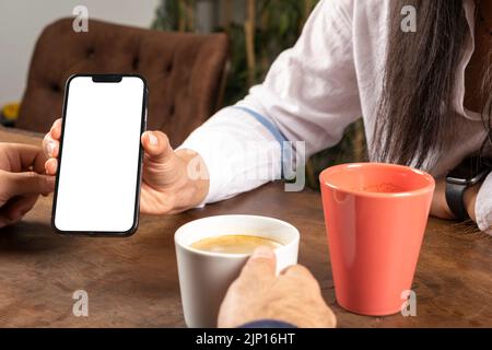 Smartphone mock up, young caucasian woman showing smartphone mock up. Couple sitting on the wooden table in cafe looking cell phone screen. Stock Photo