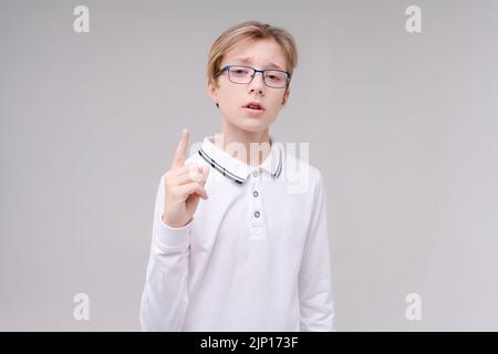 Portrait handsome caucasian boy in glasses who just has an idea points his finger in a white school t-shirt. Isolated on a gray background Stock Photo