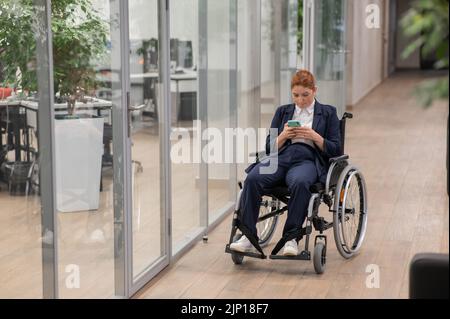 Caucasian woman using mobile phone in wheelchair at office.  Stock Photo