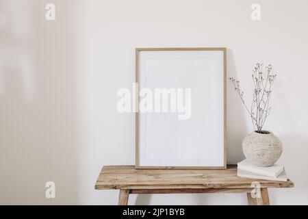 Winter, fall still life. Dry grass, plant bouquet in rustic ceramic vase. Old books on wooden bench. Blank vertical picture frame mockup. White wall Stock Photo