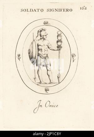 Roman standard bearer or signifer with the cohort's standard. Legoinary in crested helmet, breastplate, armour, shield or scutus, spear or hasta, standard or signum with its point in the ground. In onyx. Soldato Signifero. In onice. Copperplate engraving by Giovanni Battista Galestruzzi after Leonardo Agostini from Gemmae et Sculpturae Antiquae Depicti ab Leonardo Augustino Senesi, Abraham Blooteling, Amsterdam, 1685. Stock Photo