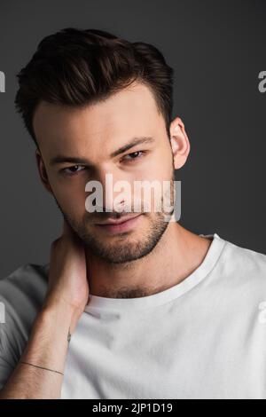 Portrait of young brunette man looking at camera while touching neck isolated on grey,stock image Stock Photo