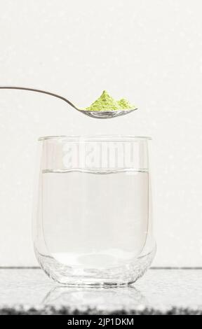 Green powder in a spoon (matcha tea) over a clear glass Stock Photo