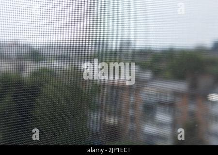 Blurred view of the city through an insect mesh on a house or apartment window. A mosquito net. Protection of housing from insects. Safety. Stock Photo