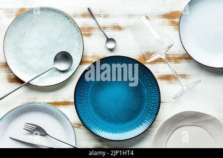 Modern tableware set with cutlery and a vibrant blue plate, with a glass for wine, overhead flat lay shot. Trendy dinnerware on a rustic background Stock Photo