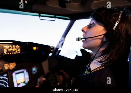 Female copilot flying plane from cockpit with dashboard command and control panel, using steering wheel and control panel for windscreen navigation. Woman using lever to fly aircraft. Stock Photo