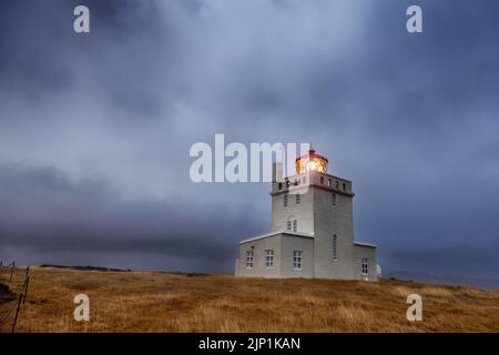 Dyrholaey Lighthouse at blue hour in autumn, the most southerly point on mainland Iceland. Storm clouds are rolling in around the mountains behind. Stock Photo