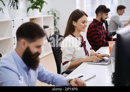 People working in modern IT office. Group of young and experienced programmers and software developers sitting at desks working on computers. Team at Stock Photo