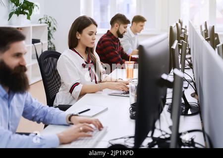 People working in modern IT office. Group of young and experienced programmers and software developers sitting at desks working on computers. Team at Stock Photo