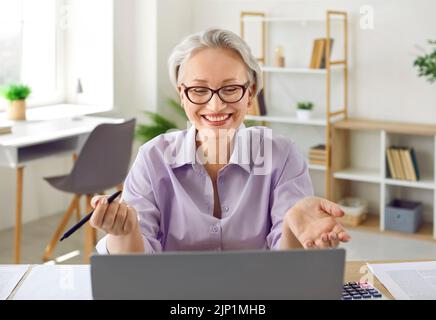 Friendly senior business woman consults with her clients using laptop web camera. Stock Photo