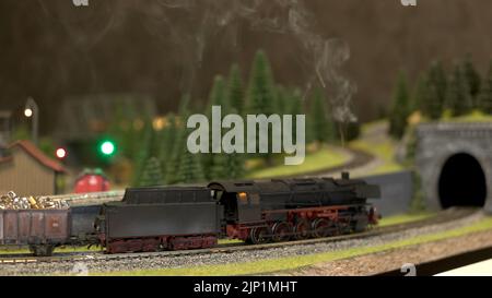 Toy train with smoke moving on model railway. Black model of locomotive with a steam. Stock Photo