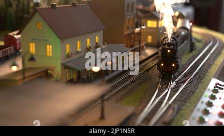 Steam engine replica entering the station. Model of steam train speeding through station. Miniature of city. Stock Photo