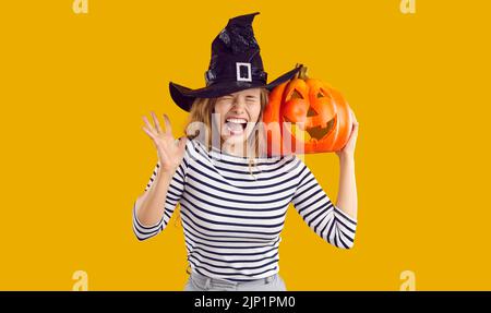 Funny, scared woman in a witch hat holding a Halloween pumpkin and screaming loudly Stock Photo