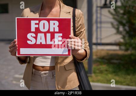 Female realtor stands with sign in her hands for sale Stock Photo