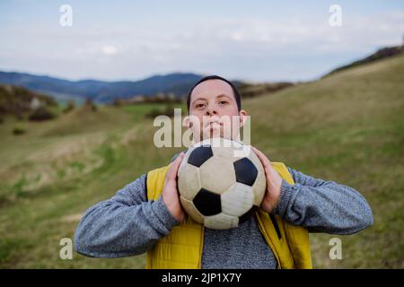 Happy young man with Down syndrome playing with soccer ball in nature. Stock Photo