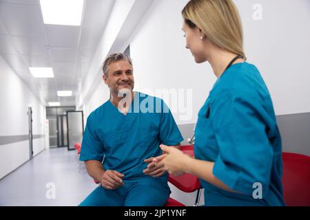 Doctors in blue uniforms are smiling and chatting with each other in the lobby of the hospital Stock Photo
