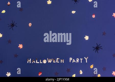 Halloween party phrase lettering made of golden letters on the dark purple blue background with autumn leaves, black stars sequins and spiders with co Stock Photo