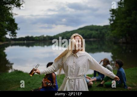 Happy young woman dancing at camping trip with friends at the lake in summer. Stock Photo