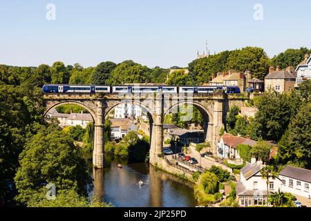 Northern trains crossing the Railway viaduct over the River Nidd, Knaresborough, North Yorkshire, England. Hot summer day with people on boats in the r Stock Photo