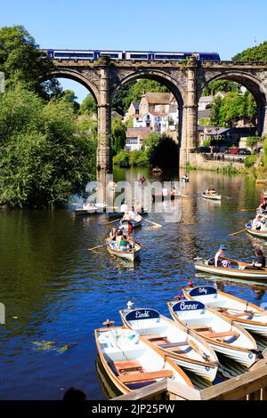 Northern trains crossing the Railway viaduct over the River Nidd, Knaresborough, North Yorkshire, England. Hot summer day with people on boats in the r Stock Photo