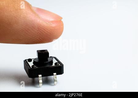 Finger is pressing small black button. Starting impulse. White background. Macro photo. Space for text. Stock Photo