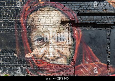 Portrait of an old man, his face framed by a cloth, painted on a dilapidated brick wall. Stock Photo