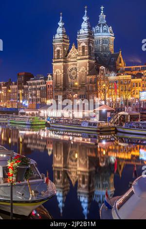 Amsterdam, Netherlands city center view with riverboats and the  Basilica of Saint Nicholas at night. Stock Photo