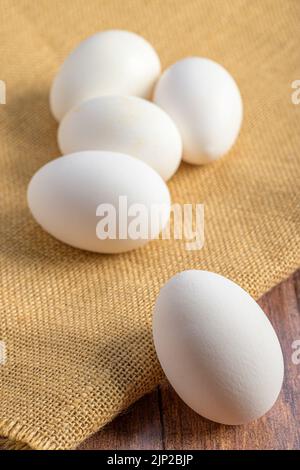 A vertical shot of four raw eggs on a wooden table in daylight Stock Photo