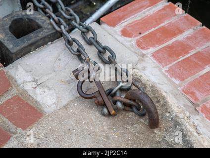 metal chain fixed to a concrete and red brick wall with D links. Stock Photo