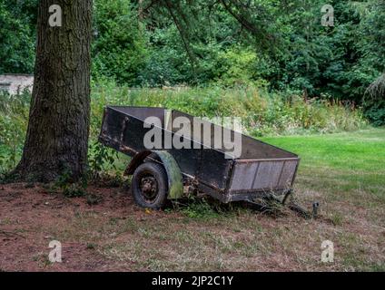 Old abandoned trailer next to a tree with over grown grass. Stock Photo