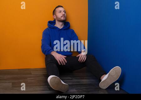 A handsome guy sitting on the floor with legs apart and head up while looking to the upper corner Stock Photo