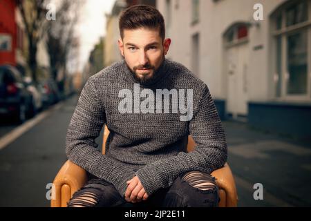 A Caucasian man sit on a chair on street while looking at camera Stock Photo