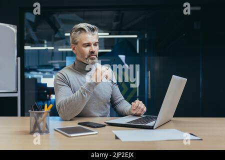 Successful and serious owner senior gray-haired investor mature businessman working in modern office using laptop, man thinking about business strategy, Stock Photo