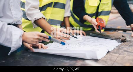 Three colleagues discussing data working with architectural project at construction site. Stock Photo