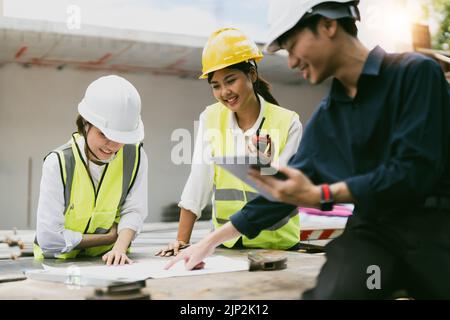 Young asian architects and engineer discussing blueprints at construction site Stock Photo