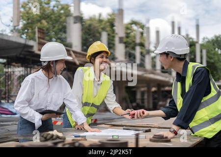 Three colleagues discussing data working and tablet, laptop with on on architectural project at construction site Stock Photo